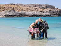 Divers in clear water with a background of rocks and beach in Shinaria Crete